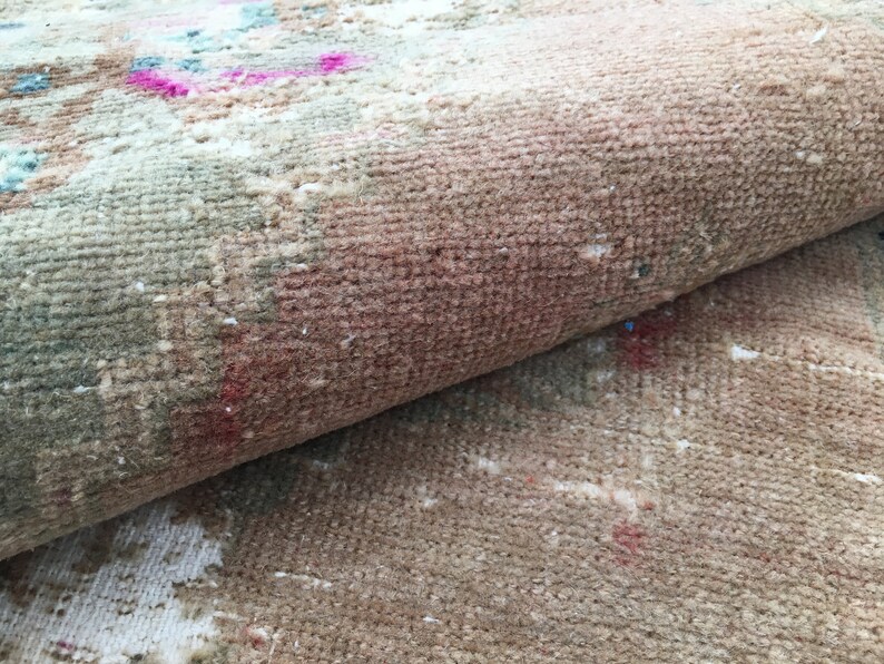 May include: Close-up of a beige and brown rug with a faded pink and blue pattern. The rug is rolled up, showing the texture of the fabric.