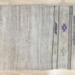 May include: A light gray rug with a woven pattern in brown, white, and purple. The rug has a fringe border.
