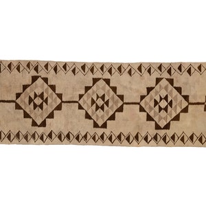May include: A long, rectangular rug with a beige background and a brown geometric pattern. The pattern features repeating diamond shapes with smaller triangles inside.