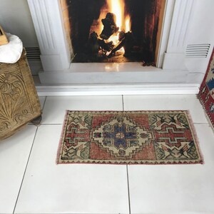 Op de afbeelding: Een rechthoekig geweven vloerkleed met een centraal blauw geometrisch medaillon omringd door ingewikkelde patronen in tinten terracotta, crème en donkergroen. Het kleed heeft korte franjes aan de uiteinden en een symmetrisch ontwerp.