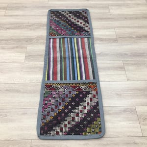 Puede incluir: Una alfombra larga y estrecha con un diseño de patchwork. La alfombra está hecha de diferentes telas con coloridos patrones geométricos. La alfombra tiene un borde gris.