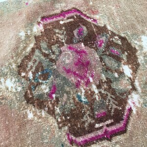 May include: A vintage rug with a faded pink and brown geometric design. The rug has a worn and distressed look, with areas of white showing through the fabric.