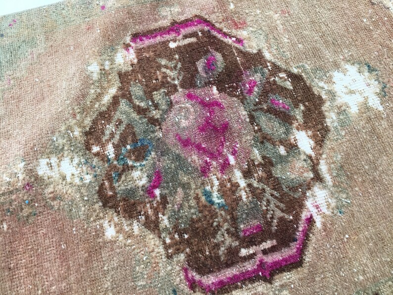 May include: A vintage rug with a faded pink and brown geometric design. The rug has a worn and distressed look, with areas of white showing through the fabric.