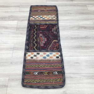 May include: A long, narrow rug with a patchwork design. The rug is made of different fabrics with various patterns in shades of red, blue, white, and brown. The rug has a dark blue border.