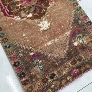 May include: A vintage brown and pink rug with a floral pattern. The rug has a faded appearance and a pink fringe.