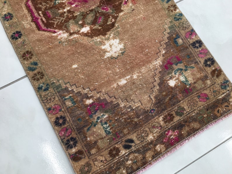 May include: A vintage brown and pink rug with a floral pattern. The rug has a faded appearance and a pink fringe.