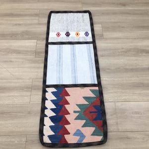 May include: A long, rectangular rug with a patchwork design. The rug has three sections: a white section with blue stripes, a gray section with colorful embroidered flowers, and a colorful section with a geometric pattern in shades of red, blue, green, and white.