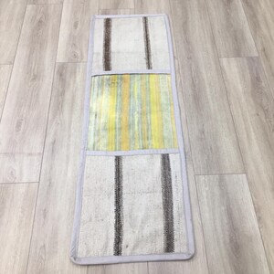 May include: A long, rectangular rug with a patchwork design. The rug is made of three different fabrics, each with a different pattern. The top section is a white fabric with black stripes, the middle section is a yellow and white striped fabric, and the bottom section is a white fabric with black stripes. The rug has a white border.