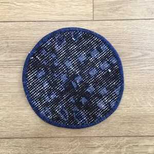 May include: A circular coaster featuring a dark navy blue and black woven textile pattern with a textured, grid-like appearance. The coaster is finished with a solid dark blue stitched border that runs along the entire outer edge of the circle.