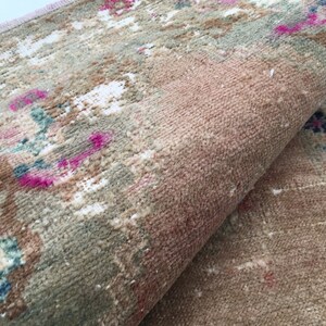 May include: A close-up of a folded rug with a faded floral pattern in shades of pink, blue, and white on a beige background.