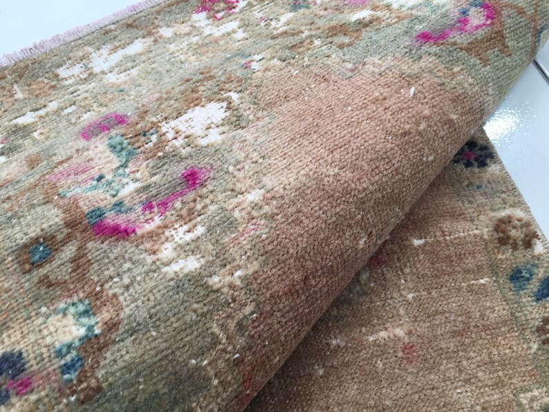 May include: A close-up of a folded rug with a faded floral pattern in shades of pink, blue, and white on a beige background.
