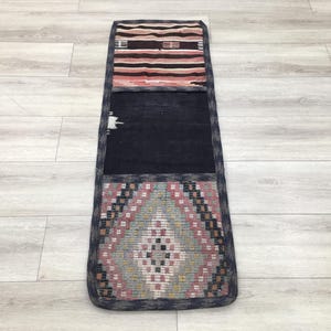 May include: A long, narrow rug with three sections. The top section is a pink and black geometric pattern, the middle section is dark blue, and the bottom section is a light pink and blue geometric pattern.