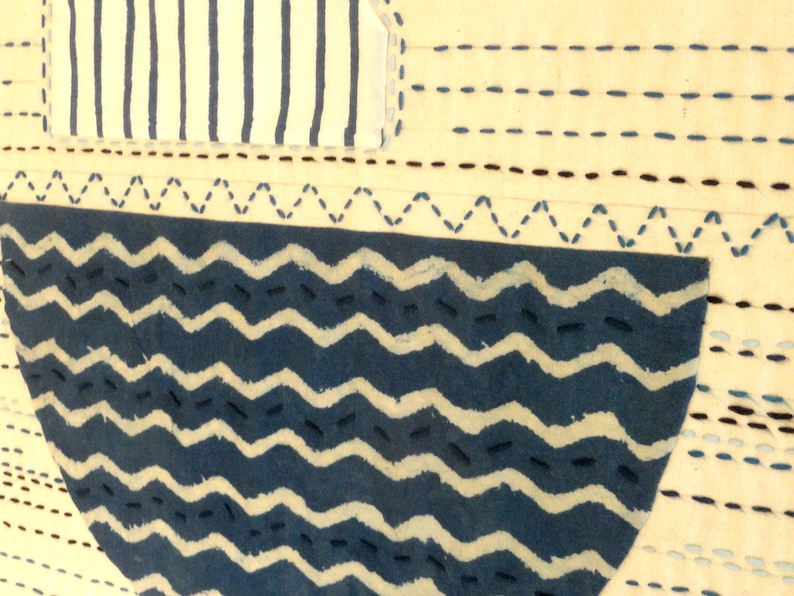 May include: A close-up of a blue and white fabric with a wavy pattern. The fabric is stitched with a running stitch in a dark blue thread. The fabric is sewn onto a cream-colored background.