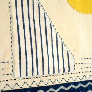 May include: A white fabric with blue stripes, stitched to form a triangle shape. The fabric is sewn to a white background with blue stitching. The bottom of the fabric has a blue and white wavy pattern.