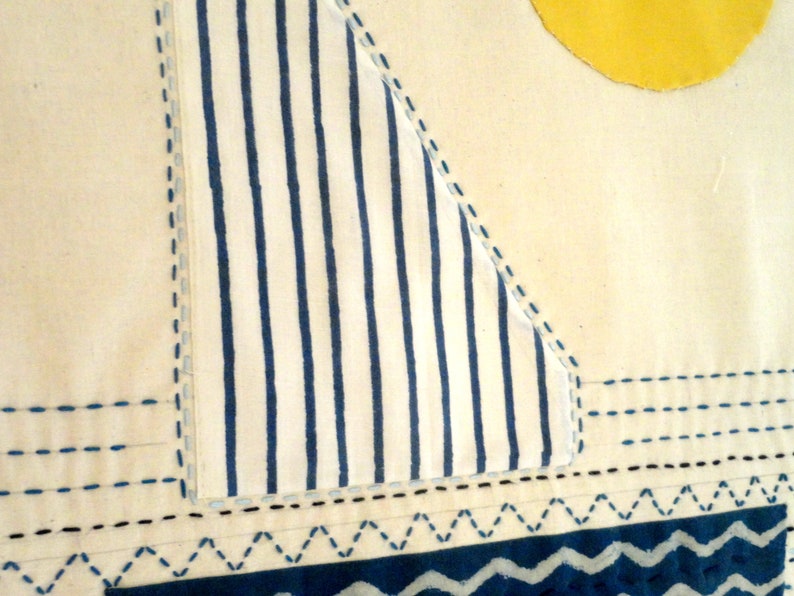 May include: A white fabric with blue stripes, stitched to form a triangle shape. The fabric is sewn to a white background with blue stitching. The bottom of the fabric has a blue and white wavy pattern.