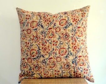 May include: A square pillow with a cream-colored background and a repeating floral pattern in red, yellow, and blue. The pillow has a quilted texture and a soft, inviting appearance. The design is reminiscent of traditional block printing.