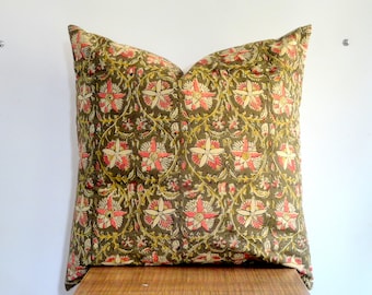 May include: A square decorative pillow with a floral pattern. The pillow features a dark olive green background with a repeating design of pink and cream-colored flowers and yellow accents. The pillow is resting on a wooden surface.