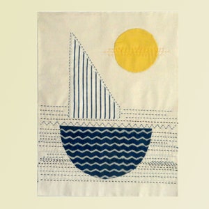 May include: A white fabric wall hanging with a blue and white striped sailboat and a yellow sun. The sailboat is on a blue and white wavy sea. The background is white with blue stitching.