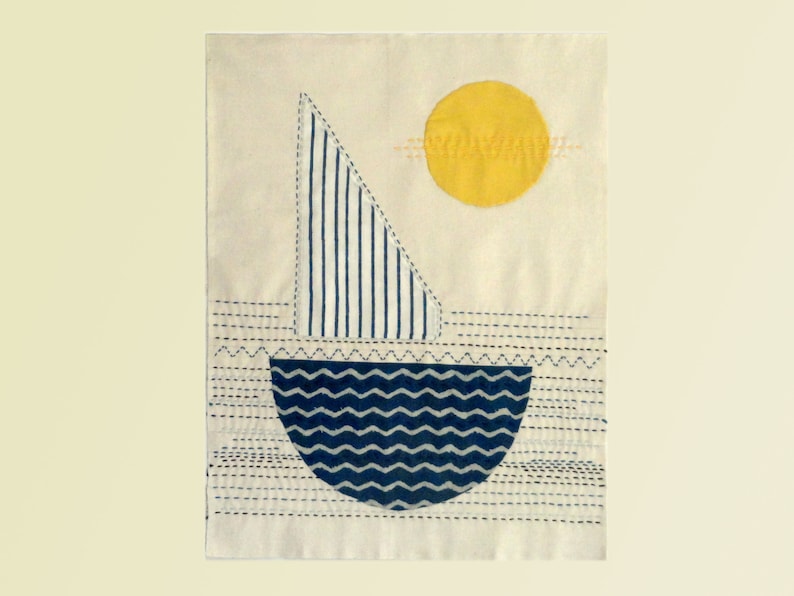 May include: A white fabric wall hanging with a blue and white striped sailboat and a yellow sun. The sailboat is on a blue and white wavy sea. The background is white with blue stitching.