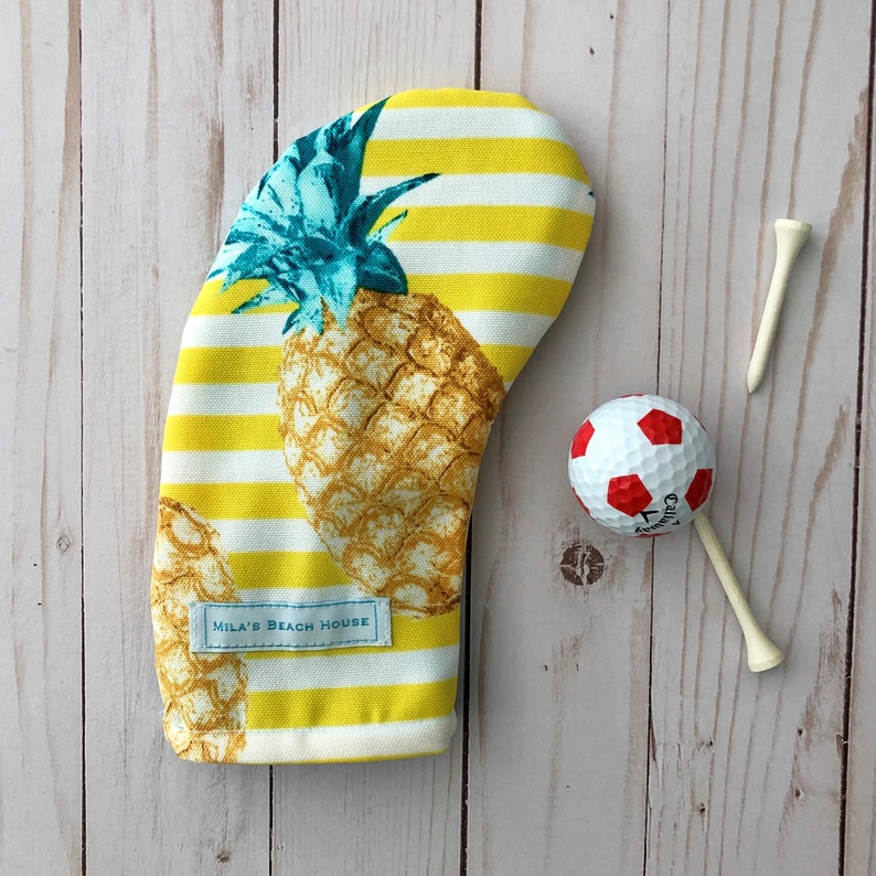 May include: Yellow and white striped golf headcover with a pineapple design and the text "Mila's Beach House".