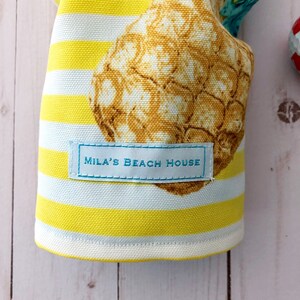 May include: Yellow and white striped fabric with a pineapple print and a blue label that says "Mila's Beach House".