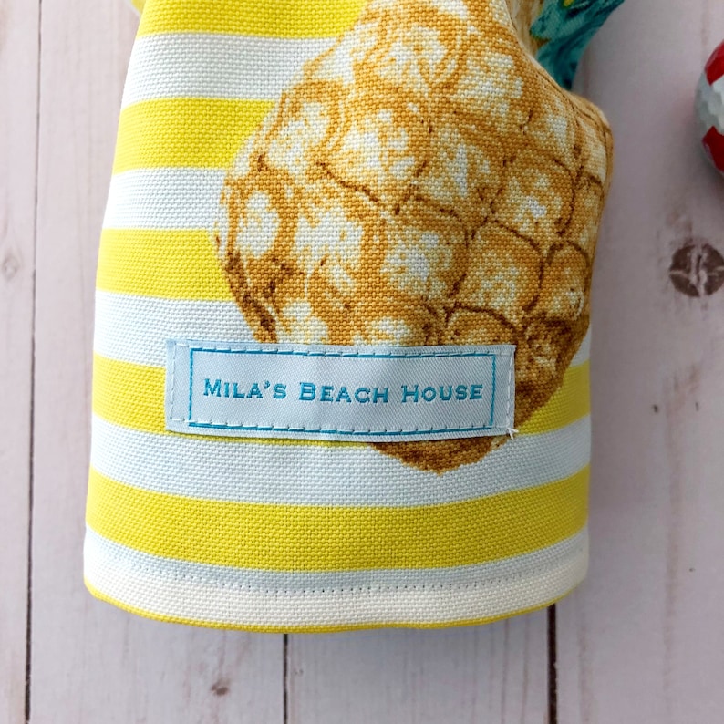 May include: Yellow and white striped fabric with a pineapple print and a blue label that says "Mila's Beach House".