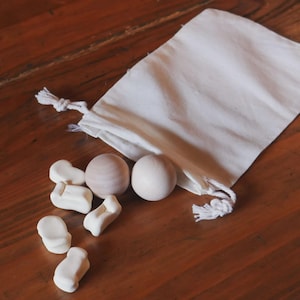 May include: A small, off-white drawstring bag with a collection of wooden toys. The toys include two spheres and several small, white, chair-shaped pieces. The items are arranged on a dark wooden surface.