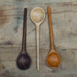 May include: Three wooden spoons of different colors and wood grains. The spoons are arranged in a row on a wooden surface.