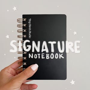 Peut inclure: Un carnet à spirales noir avec une reliure en fil de couleur cuivre. La couverture présente le texte Tiny Birch Studio verticalement sur le côté gauche et le mot SIGNATURE en grandes lettres blanches au-dessus du mot NOTEBOOK en lettres plus petites.