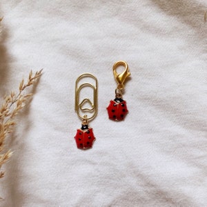 May include: Two gold ladybug charms, one attached to a gold paper clip and the other to a gold lobster clasp.