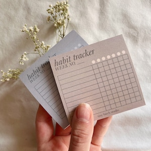 May include: Two habit tracker sheets with a gray and beige color scheme. The top sheet has the text "habit tracker" and "week no." The bottom sheet has the text "tiny birch studio".