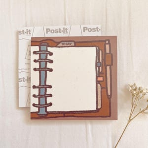 May include: A brown leather-bound planner with a white page open and the word "TODAY" written on a tab. The planner has a ring binder and a pen is sticking out of the side.
