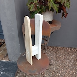 May include: A white and natural wood coat rack with two hooks. The rack is standing on a rusty metal stool.