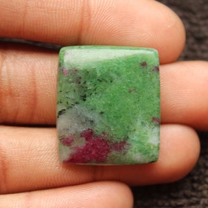 Puede incluir: Una piedra preciosa rectangular de cabujón verde y rosa con una superficie lisa y pulida.