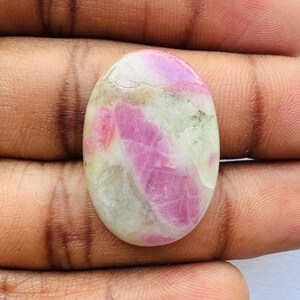 Pu&ograve; includere: Pietra preziosa ovale con una miscela di rosa e bianco sporco. Le sezioni rosa sono prominenti, creando un contrasto sorprendente con lo sfondo pi&ugrave; chiaro. La pietra ha una superficie lucida e riflette la luce.