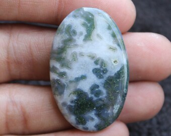 Pode incluir: Um cabochão de ágata verde e branco com um padrão de redemoinho. O cabochão tem forma oval e uma superfície lisa e polida.