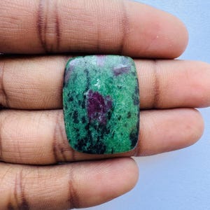 Può includere: Una gemma rettangolare con una superficie lucida. La pietra presenta un mix di colori verde e rosso scuro. Le aree verdi hanno macchie nere e le aree rosse sono concentrate al centro.