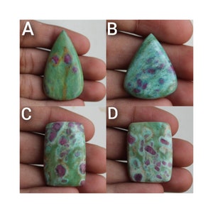 Puede incluir: Se muestran cuatro piedras preciosas en cabujón, etiquetadas como A, B, C y D, en una mano. Las piedras preciosas son verdes con inclusiones rosadas y blancas. Las piedras preciosas tienen forma de lágrima para A y B, y forma rectangular para C y D.