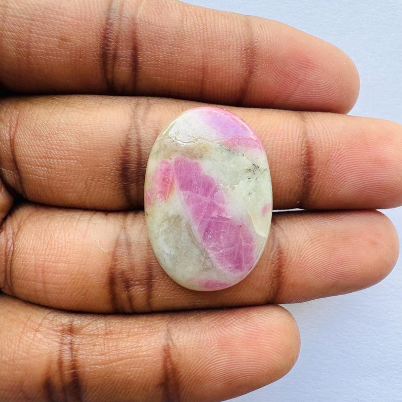 Pu&ograve; includere: Pietra preziosa ovale con una miscela di rosa e bianco sporco. Le sezioni rosa sono prominenti, creando un contrasto sorprendente con lo sfondo pi&ugrave; chiaro. La pietra ha una superficie lucida e riflette la luce.