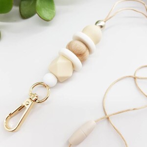 May include: A beige and white beaded lanyard with a gold metal clip and a beige wooden bead at the end.