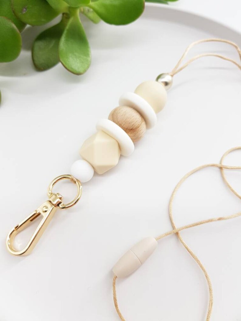 May include: A beige and white beaded lanyard with a gold metal clip and a beige wooden bead at the end.