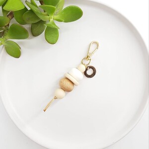 May include: A wooden bead keychain with a gold clasp and a small gold charm. The beads are in shades of brown, beige, and white.