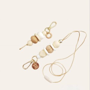 May include: A beige and white beaded lanyard with a gold clasp and a small gold charm. The lanyard has a wooden bead with the text "Touch Love More" engraved on it.