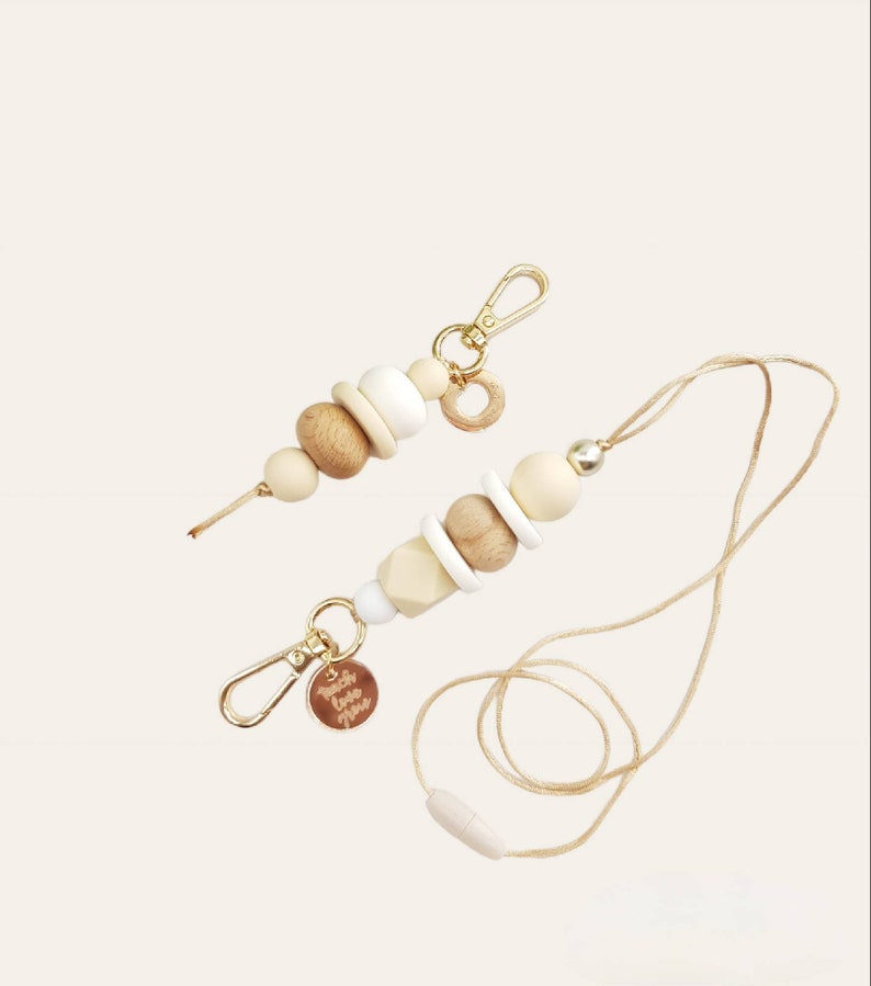 May include: A beige and white beaded lanyard with a gold clasp and a small gold charm. The lanyard has a wooden bead with the text "Touch Love More" engraved on it.