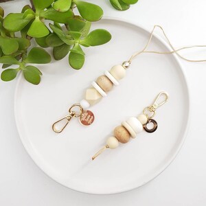 May include: Two wooden bead keychains with gold accents. One keychain has a small gold charm with the text "Love You" on it. The other keychain has a small gold circle charm.