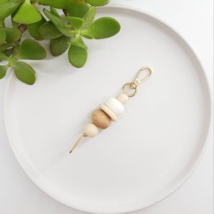 May include: A wooden bead keychain with a gold metal clasp. The beads are in shades of brown and white.