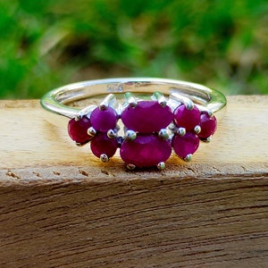 May include: A silver ring with five oval-shaped ruby gemstones set in a cluster.