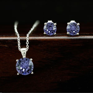 Puede incluir: Un conjunto de collar y pendientes de plata con un colgante redondo de piedra preciosa de color p&uacute;rpura oscuro y pendientes a juego.