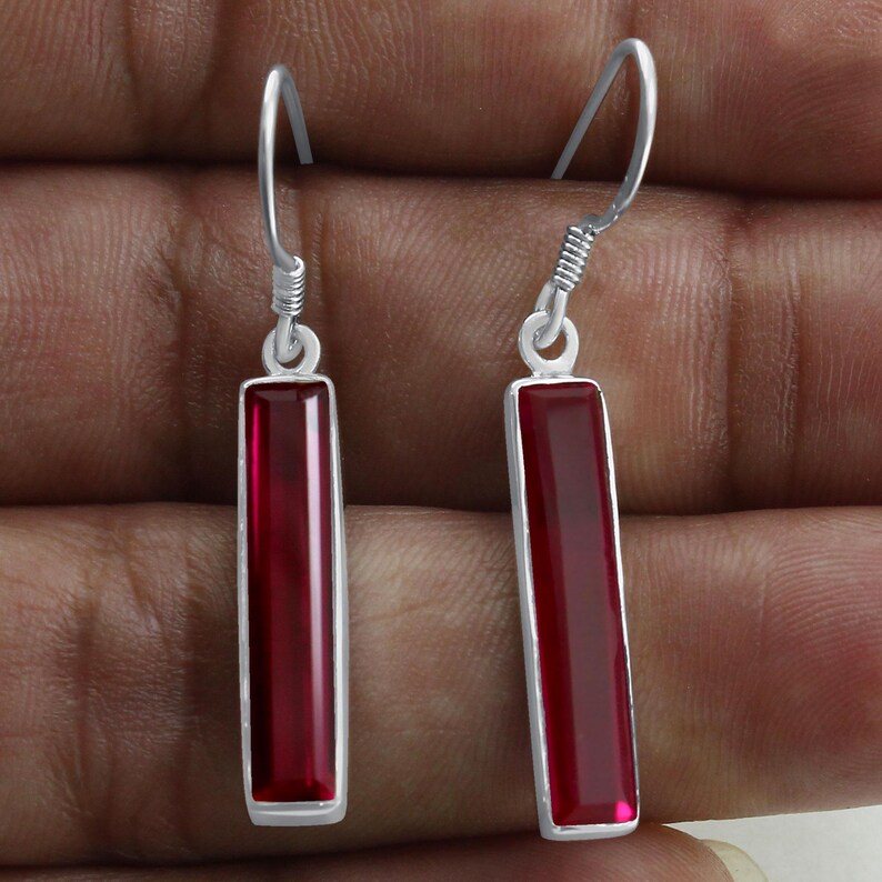 May include: A pair of silver dangle earrings with red rectangular gemstones. The earrings have a simple design and are perfect for everyday wear.