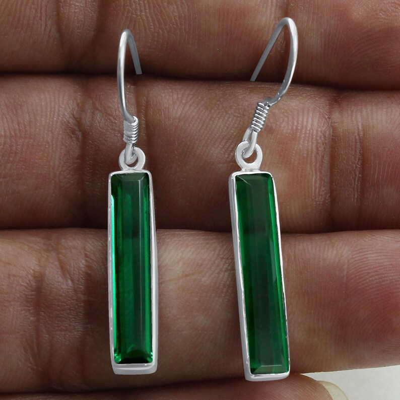 May include: A pair of silver dangle earrings with green rectangular gemstones. The earrings have a simple design and are perfect for everyday wear.